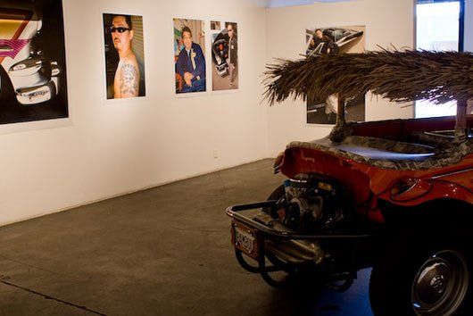 A red car with a thatched roof is in a room with paintings on the wall