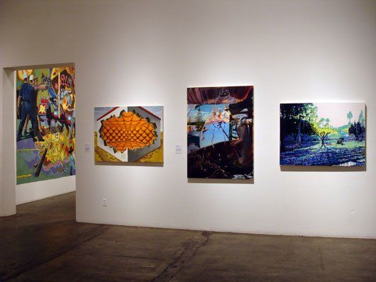 Three paintings are hanging on a wall in a museum