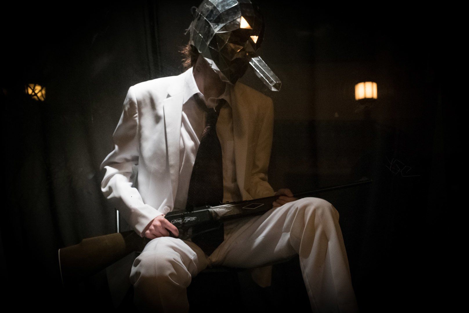 A man in a suit and tie is sitting in a dark room with a mask on his head.