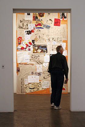 A man is standing in front of a wall with a lot of papers on it.