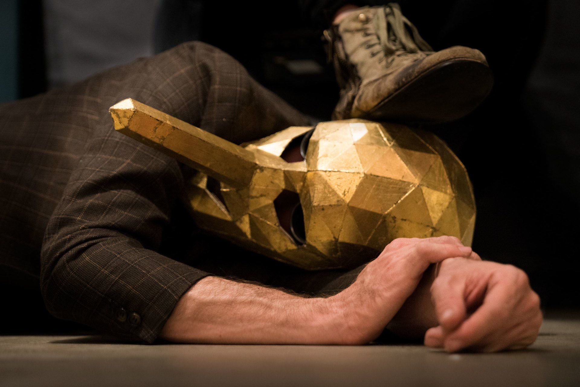 A man wearing a gold mask is laying on the floor.