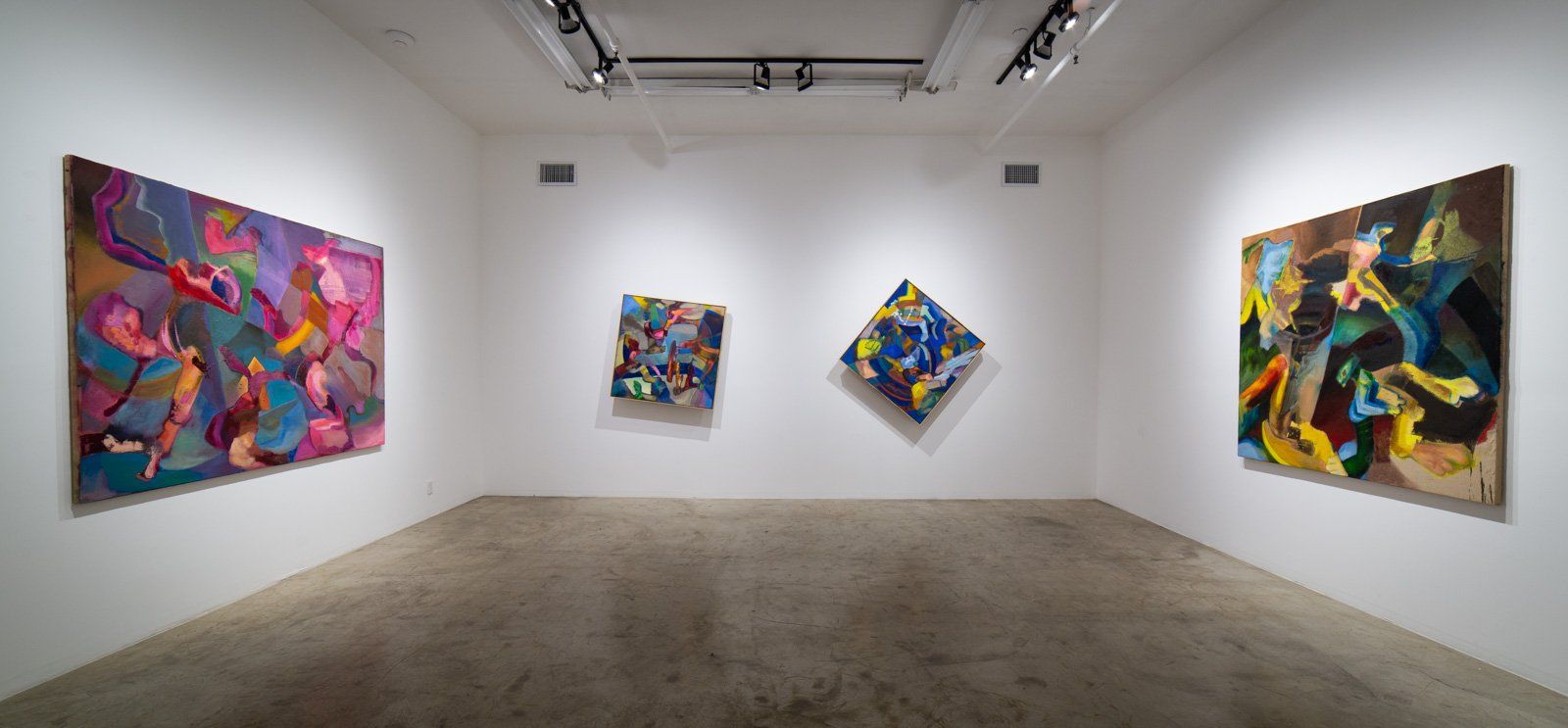 A room with three paintings on the wall and a concrete floor.
