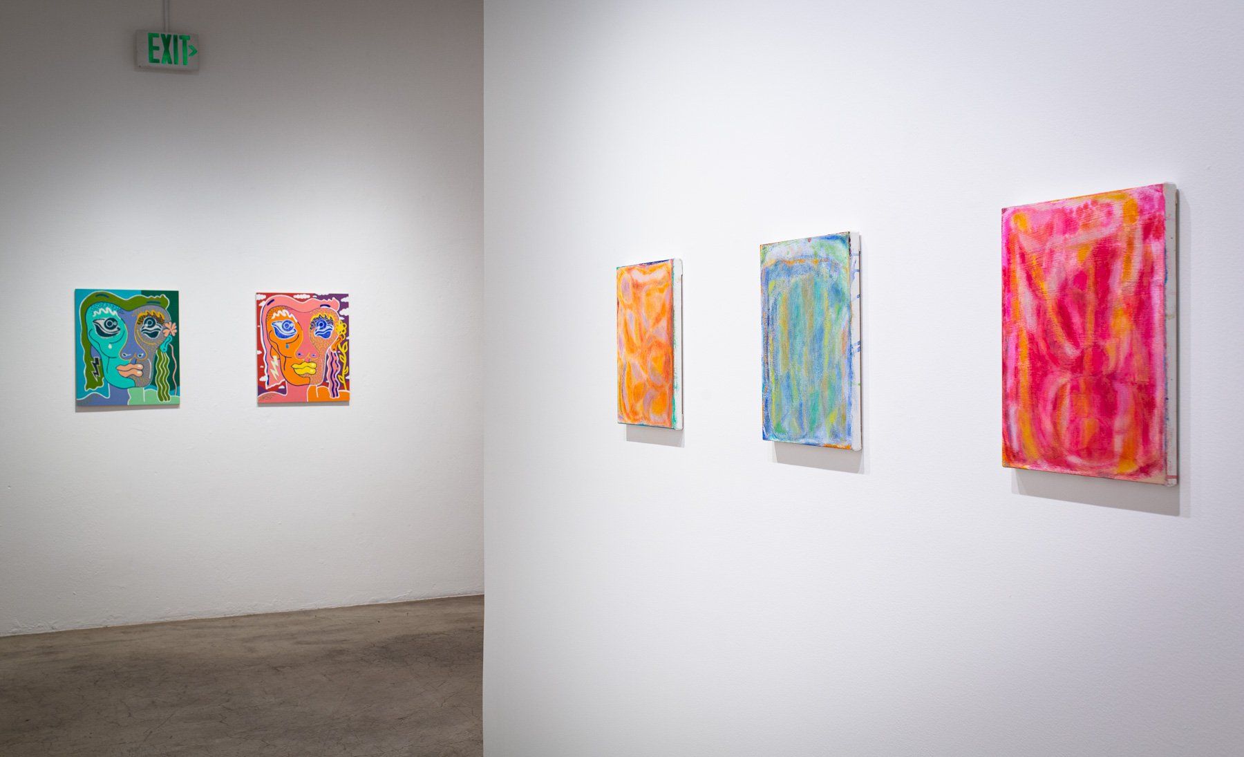 A row of colorful paintings are hanging on a white wall in Track 16 Gallery.