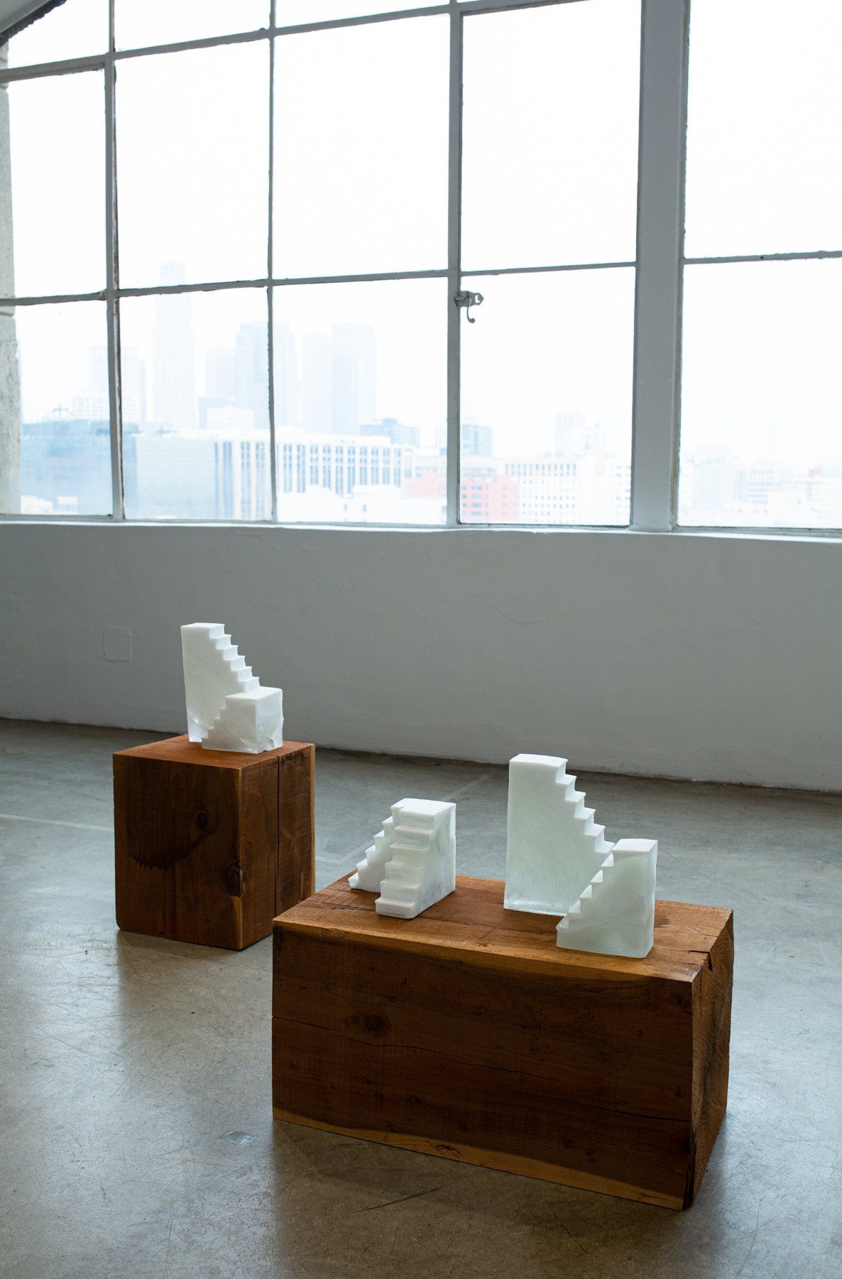 Three sculptures are sitting on wooden blocks in front of a window.