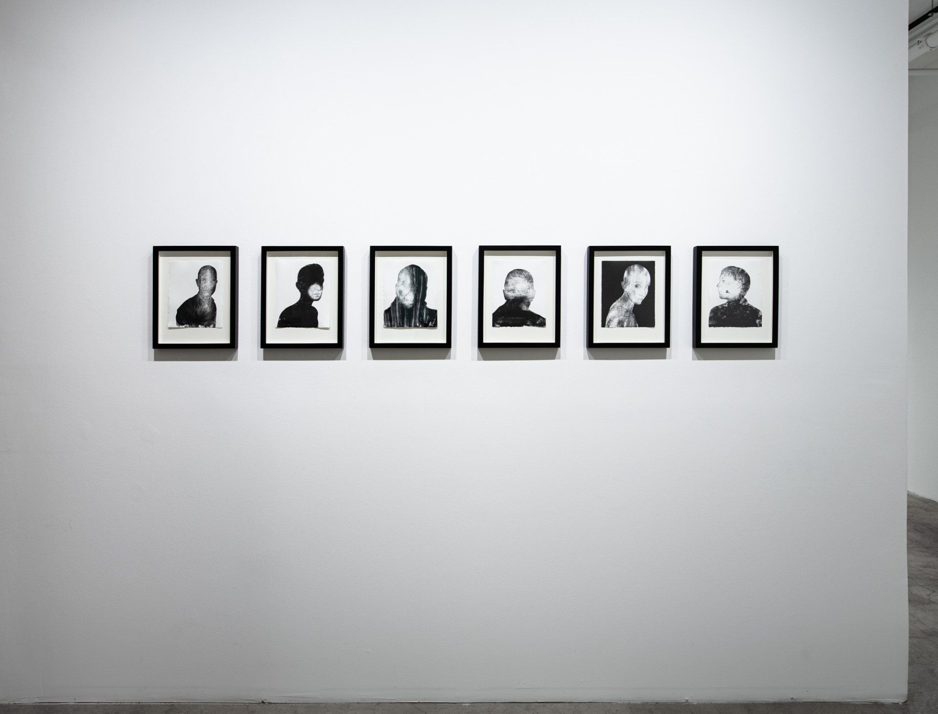 A row of black and white portraits are hanging on a white wall.