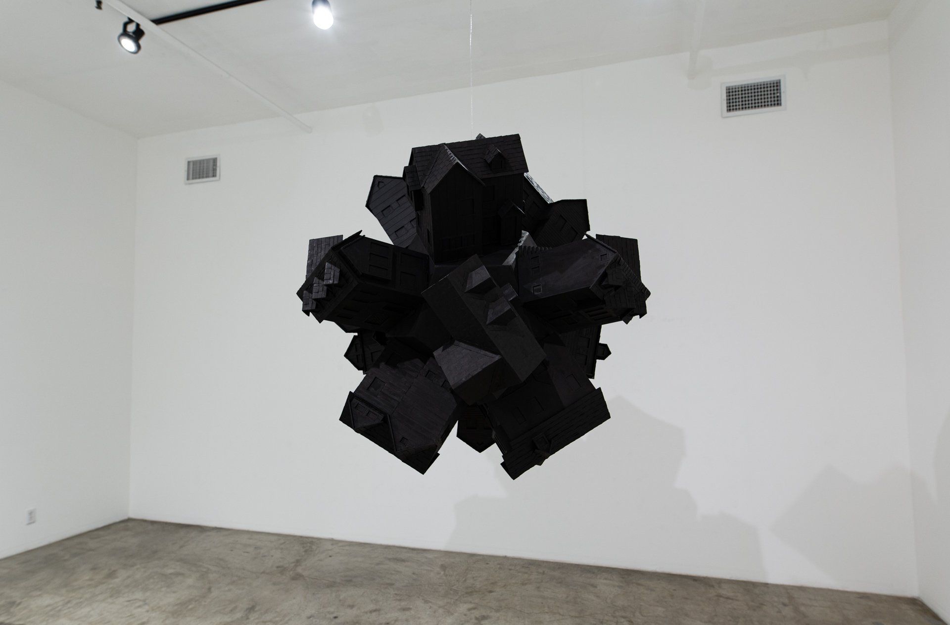A large black sculpture is hanging from a white wall in a room.