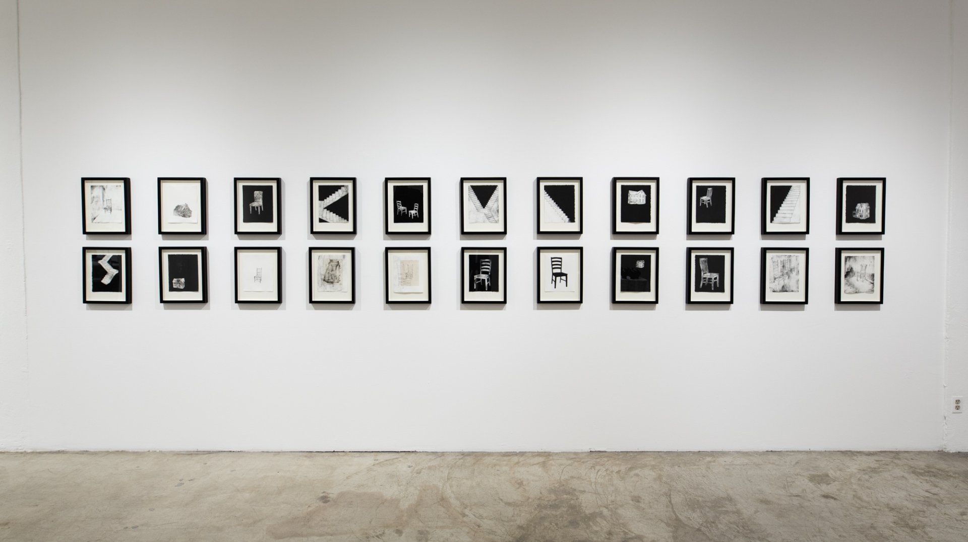 A row of black and white paintings on a wall in a museum.