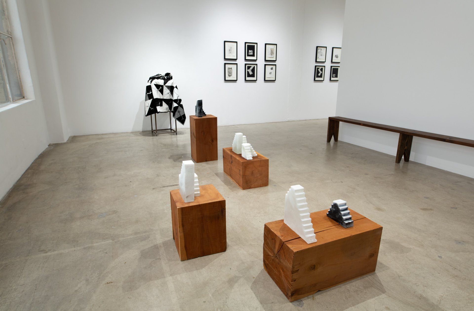 A room with a lot of sculptures on wooden blocks and a bench.