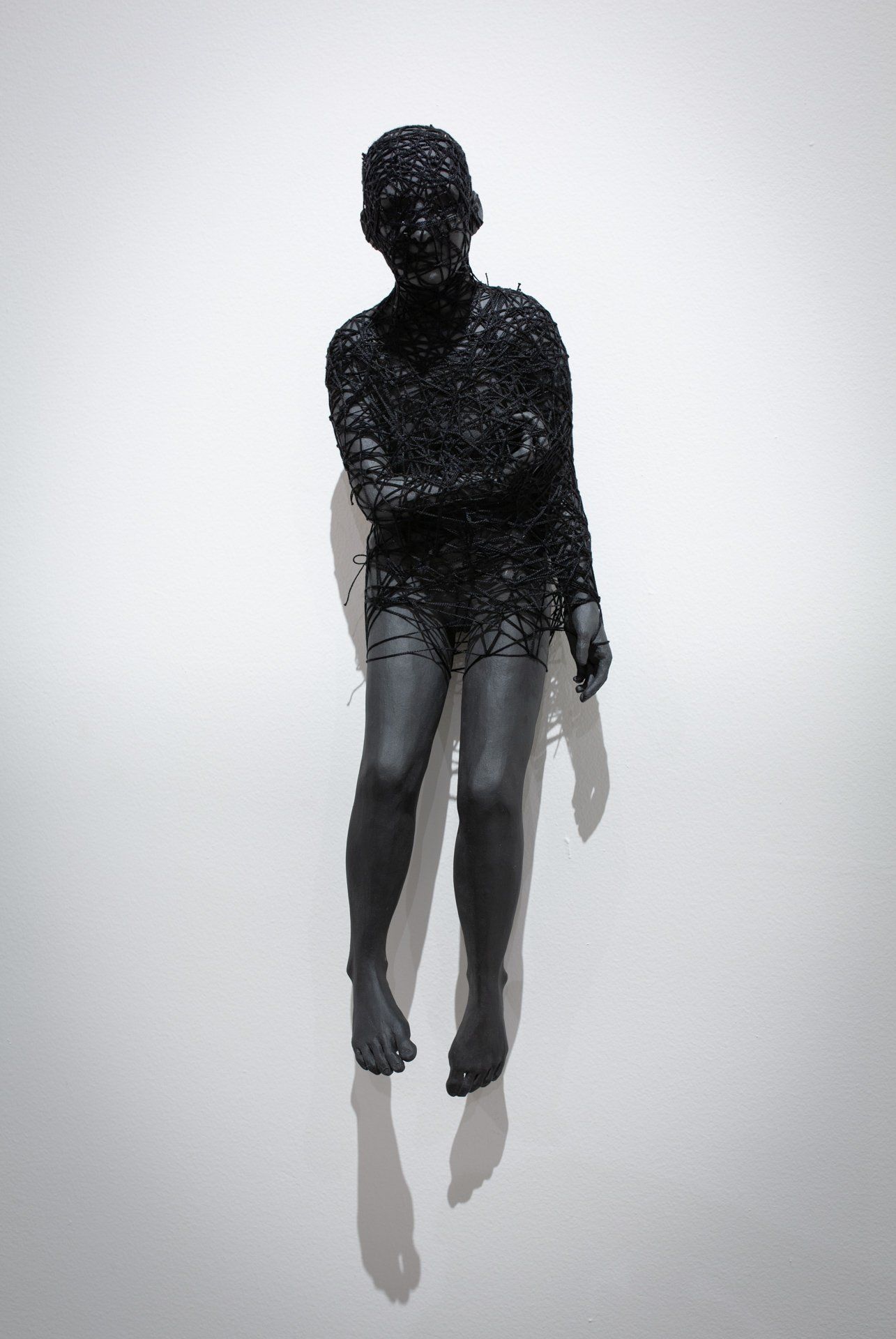A black statue of a person sitting on a white wall.