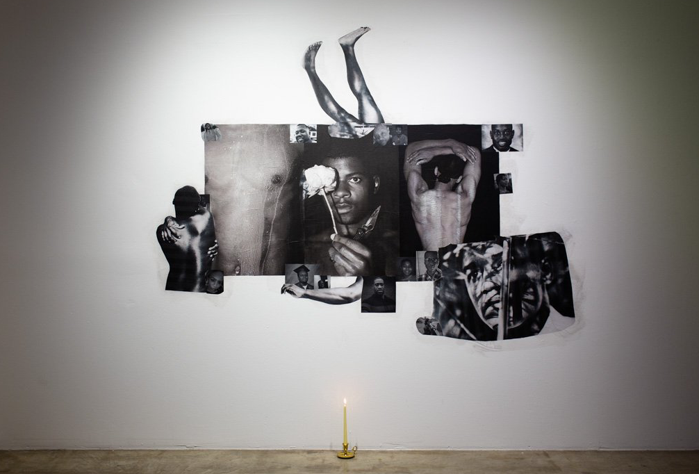 A candle is lit in front of a collage of pictures on a wall.