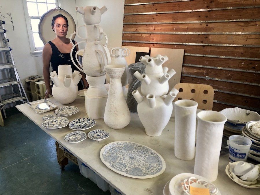 A woman is standing in front of a table filled with vases and plates.