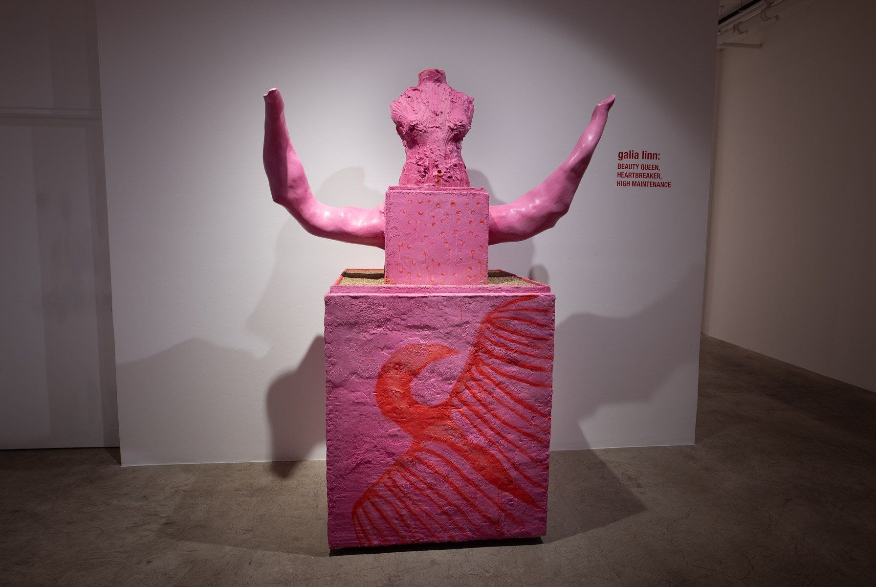 A pink statue is sitting on top of a pink box in a room.
