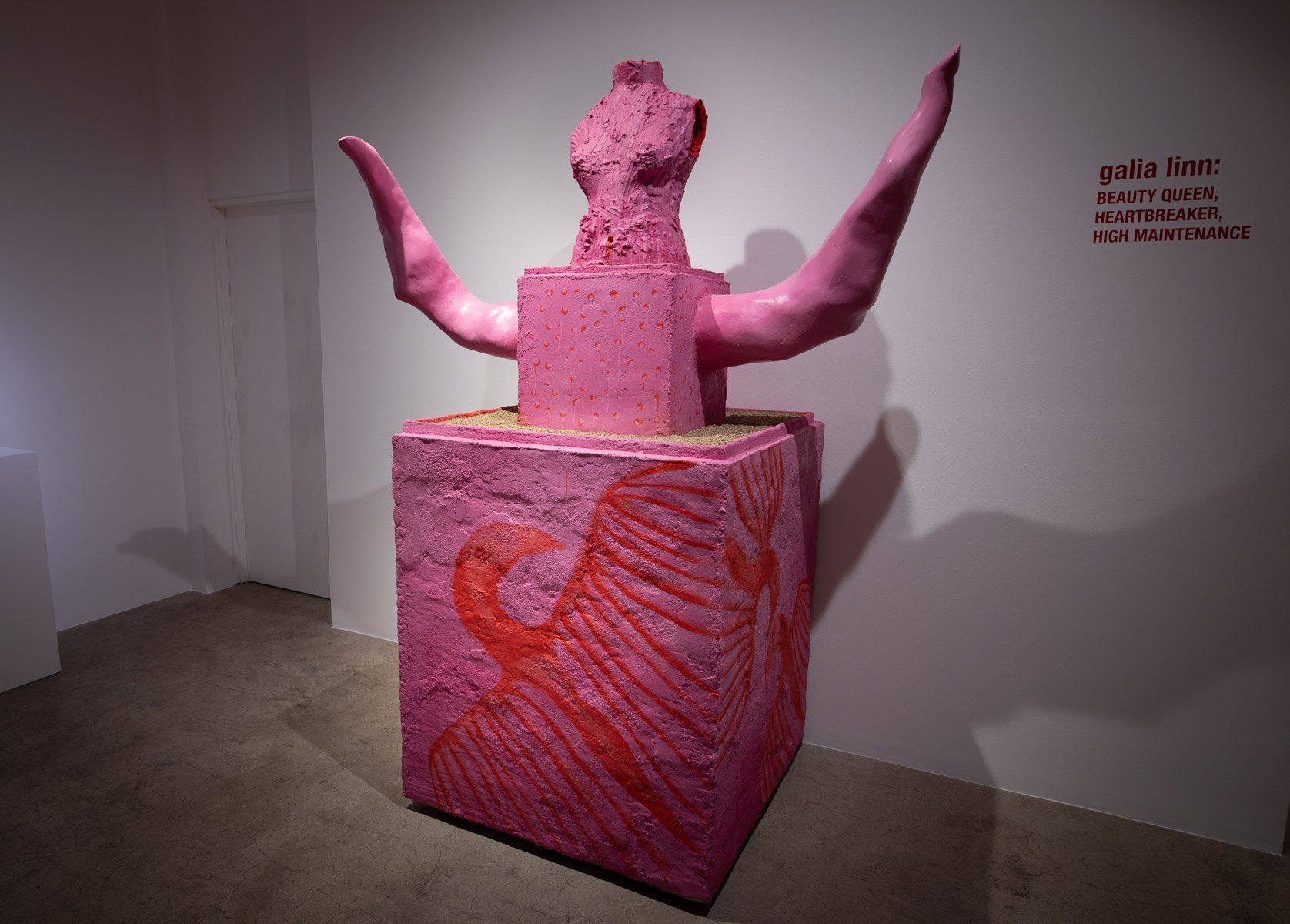 A pink statue is sitting on top of a pink cube in a room.