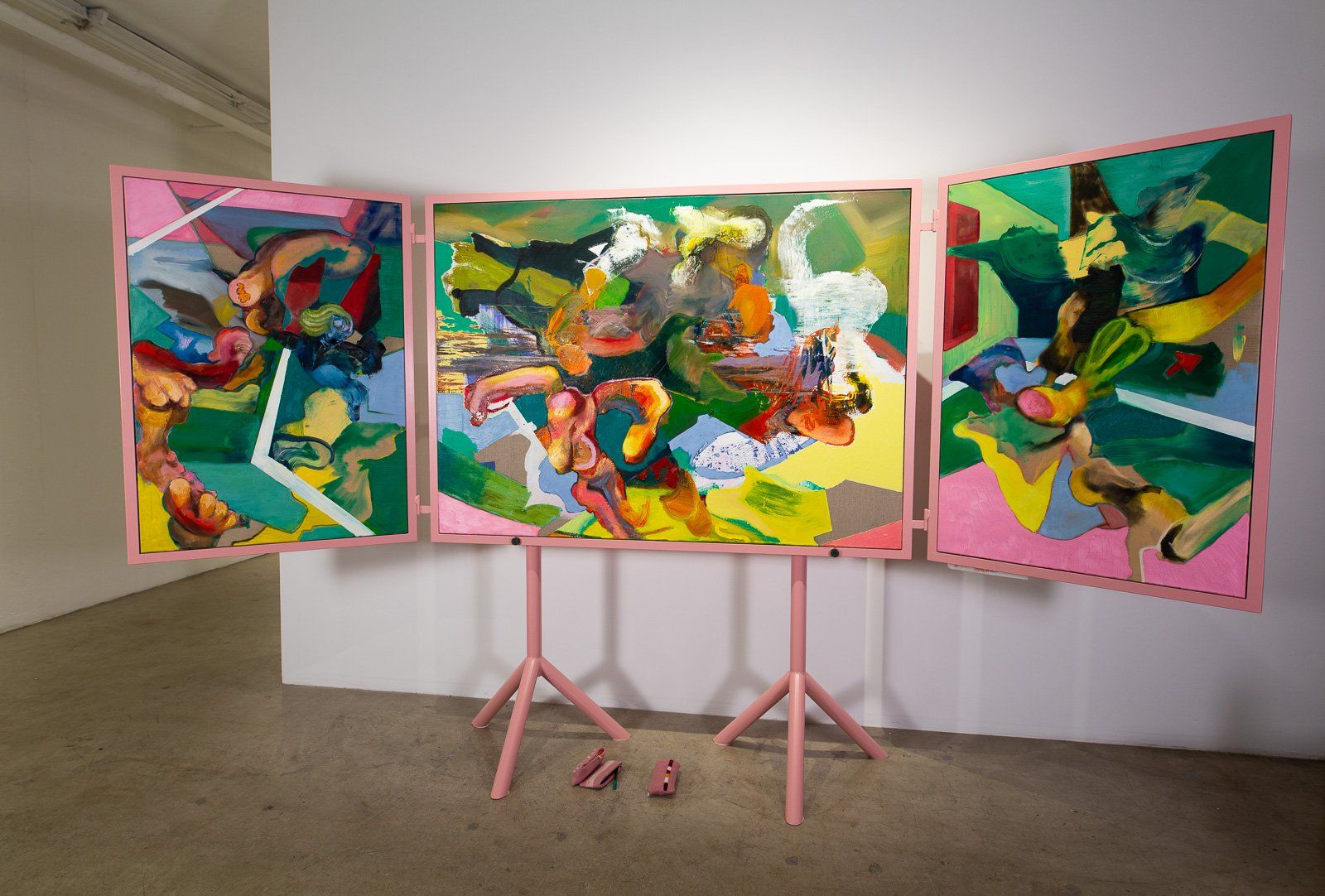 Three paintings are displayed on a pink stand in a room.