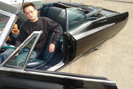 A man is sitting in the back seat of a black convertible car.