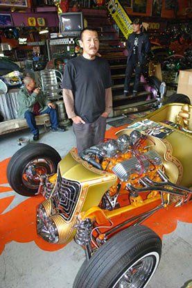 A man is standing next to a gold car in a garage.
