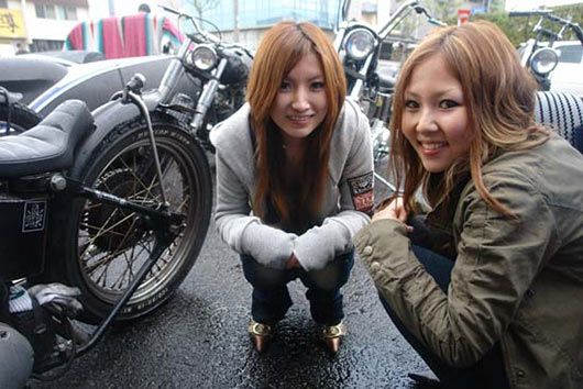 Two women are posing for a picture in front of a motorcycle.