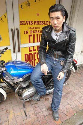 A man in a leather jacket is sitting on a motorcycle.