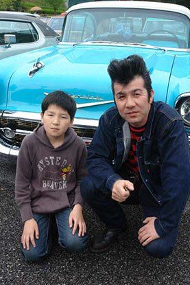 A man and a boy are posing for a picture in front of a blue car.