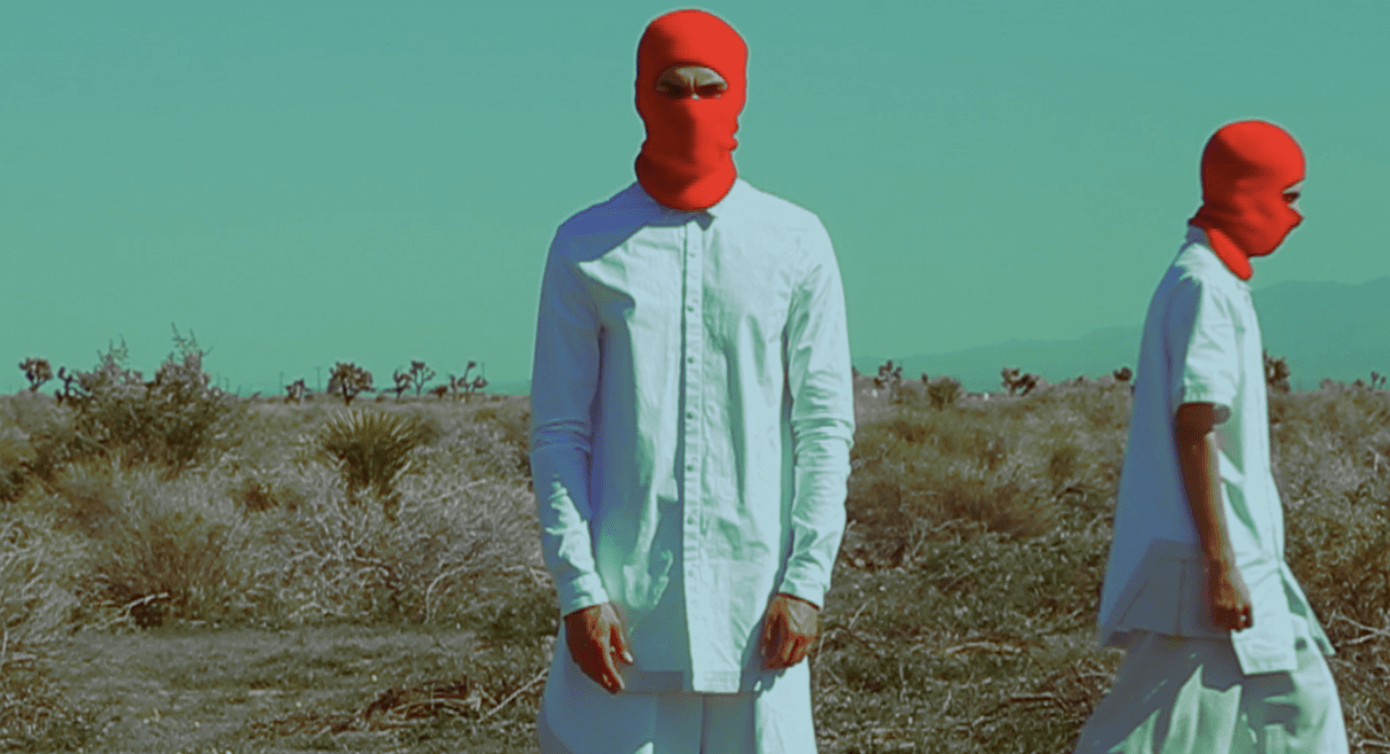Two people wearing red masks are standing in a field.