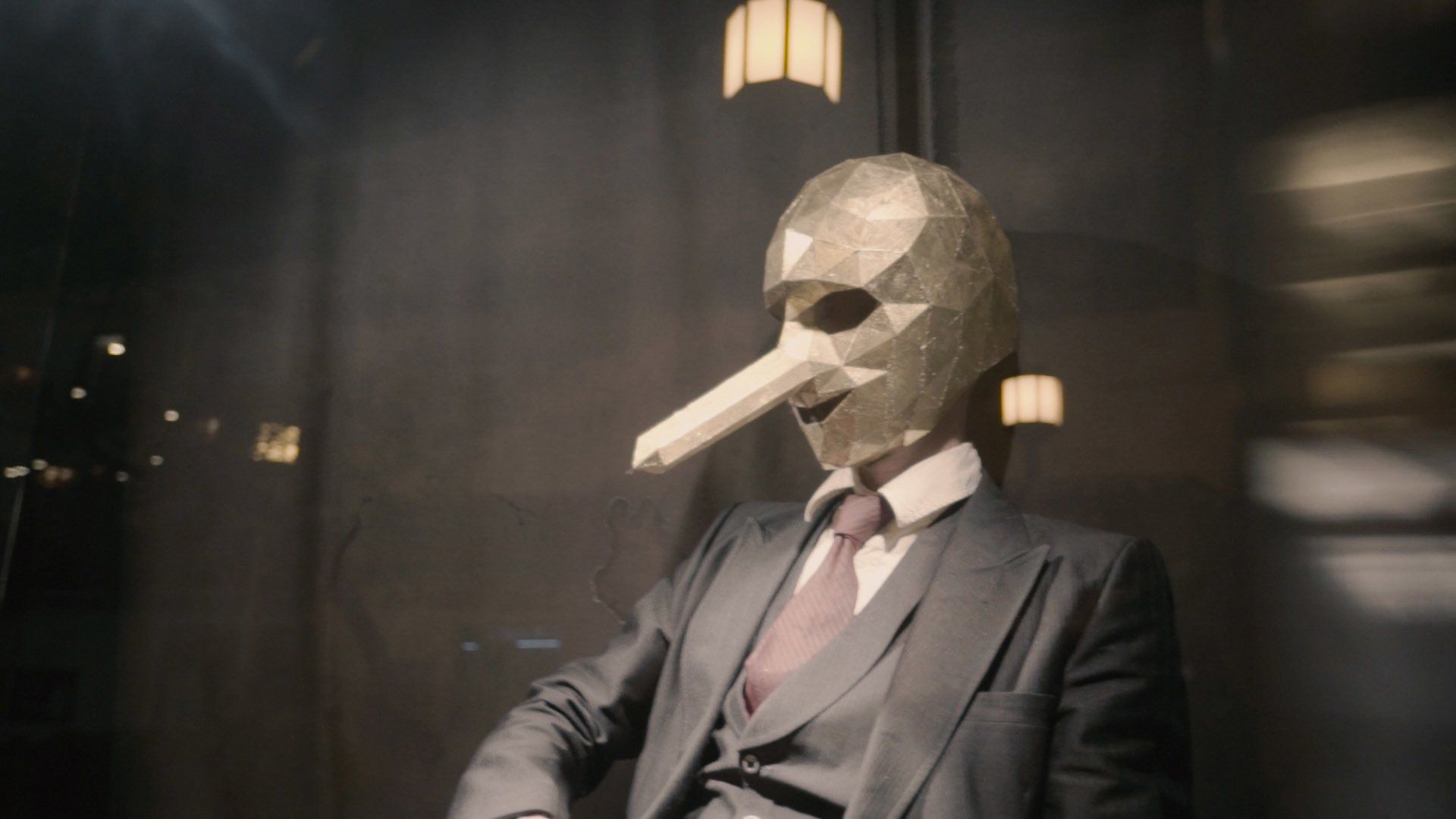 A man in a suit and tie is wearing a long nose mask.