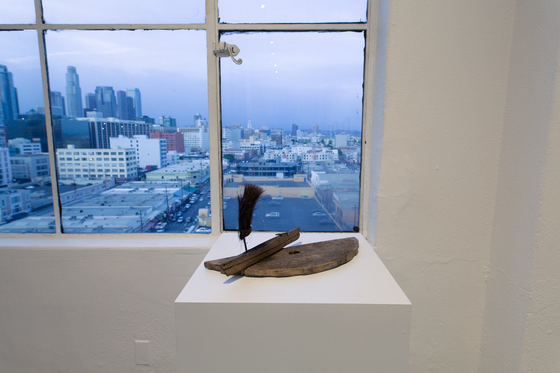 A sculpture is sitting on a shelf in front of a window with a view of a city.