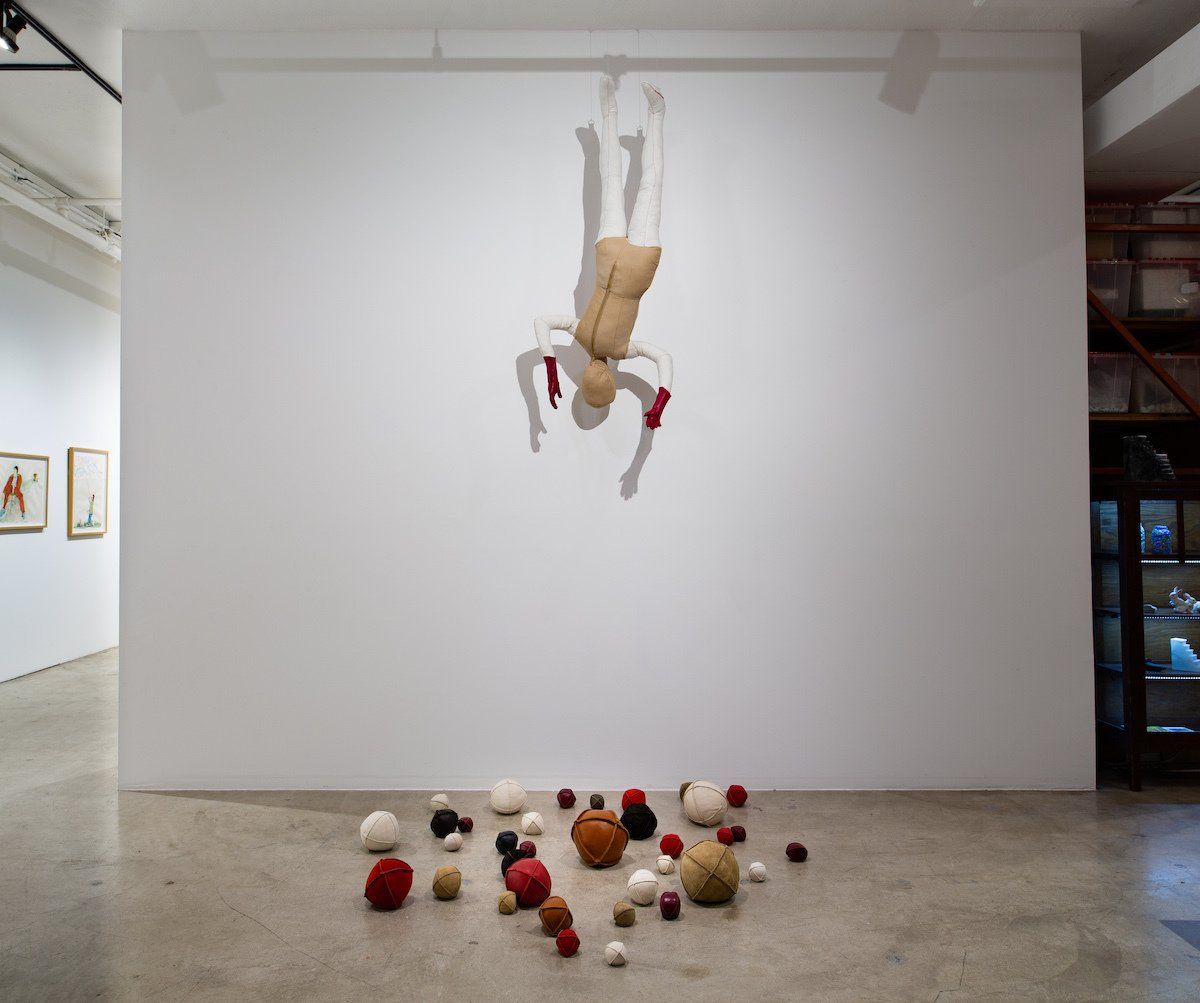 A sculpture of a person doing a handstand is hanging from a wall in a museum.