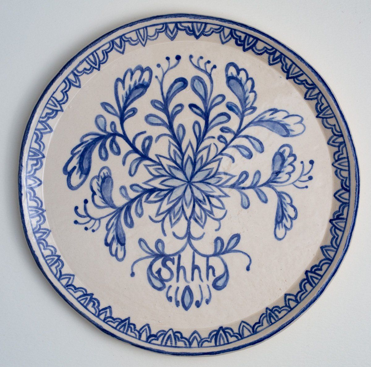 A blue and white plate with the word shh on it