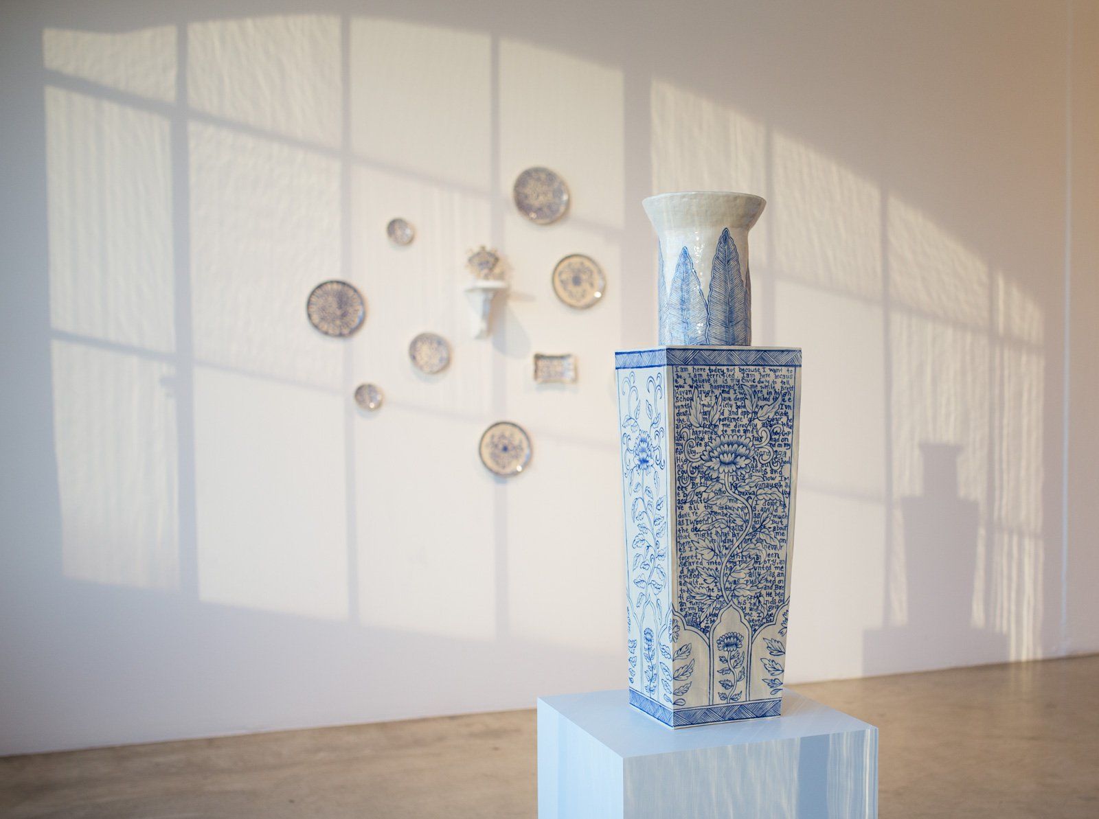 A blue and white vase is sitting on a pedestal in front of a window.