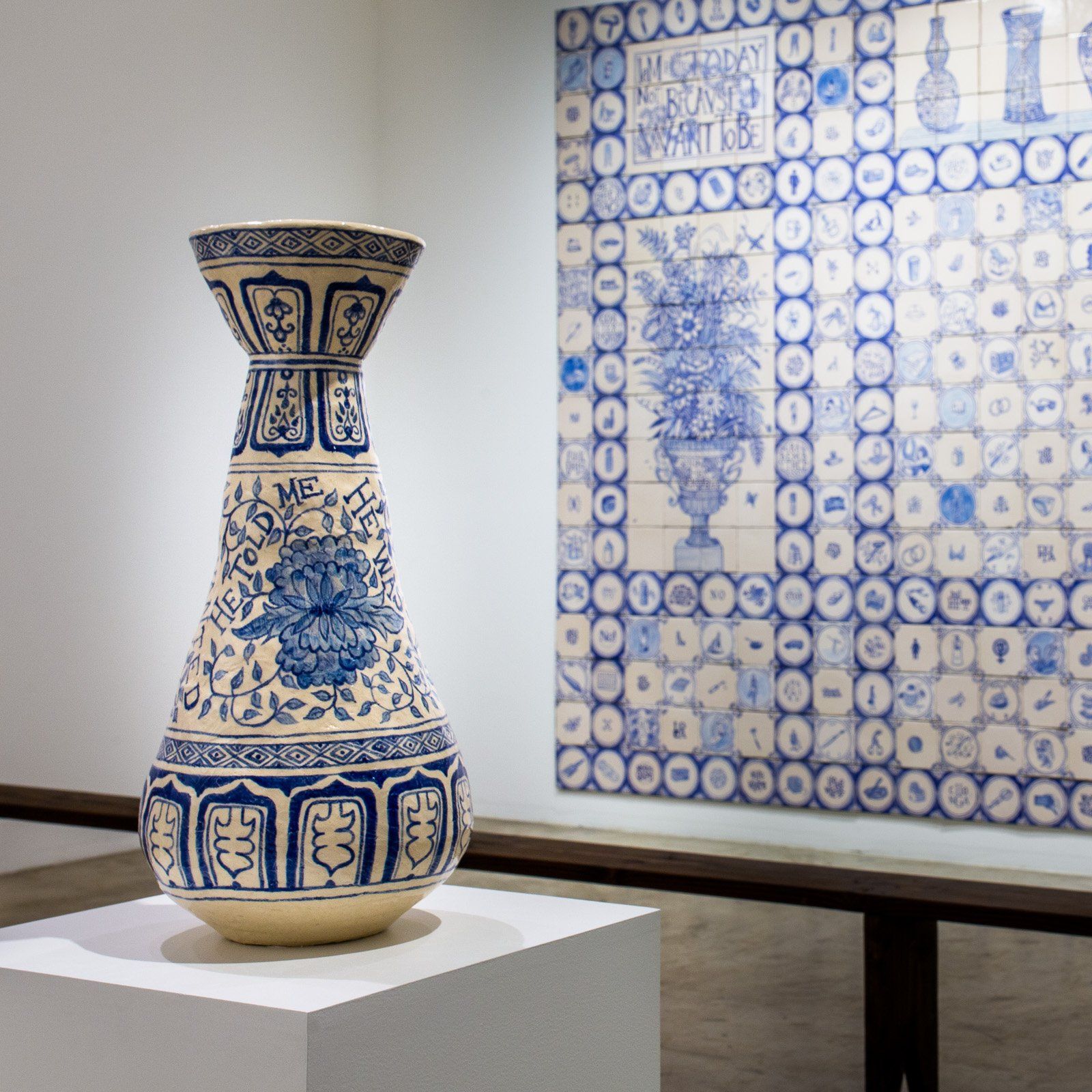 A blue and white vase is on display in front of a tiled wall