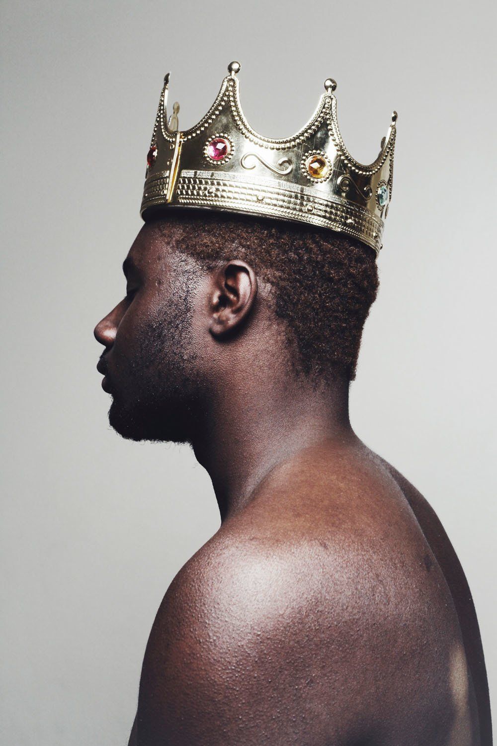A man without a shirt is wearing a gold crown