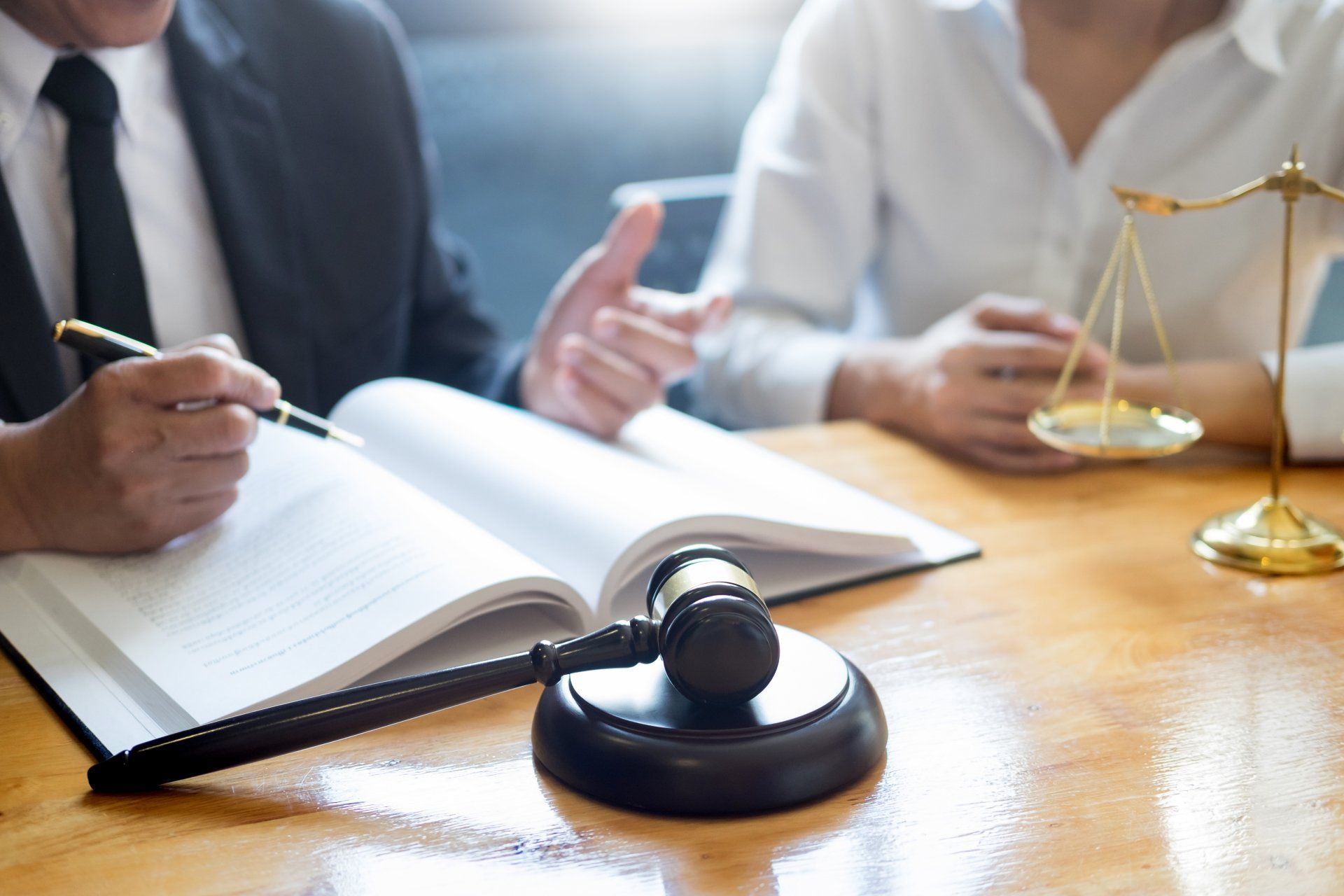 Lawyer explaining to client, legal book, gavel, scales of justice on desk.