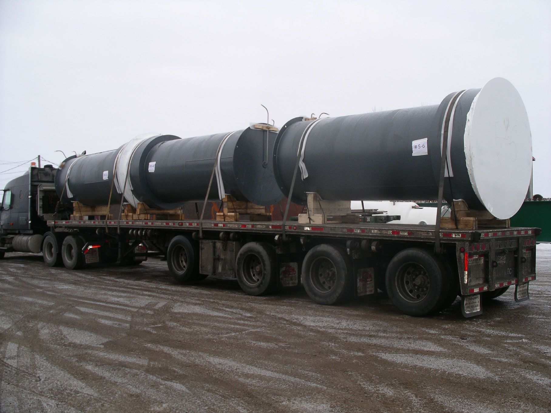 Un semi-remorque transporte de gros tuyaux sur une remorque à plateau.