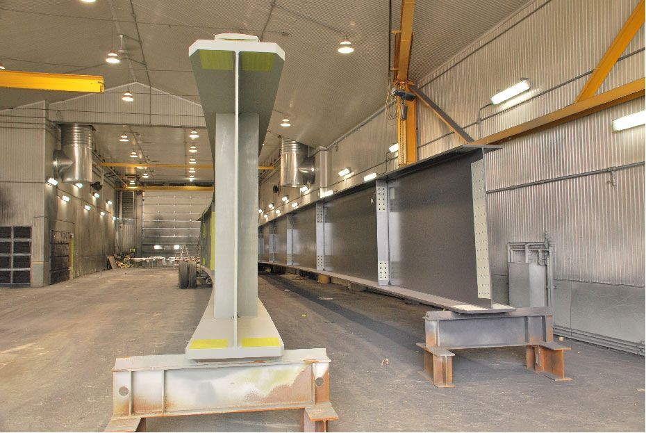 Une grande structure métallique est en train d'être peinte dans une usine.