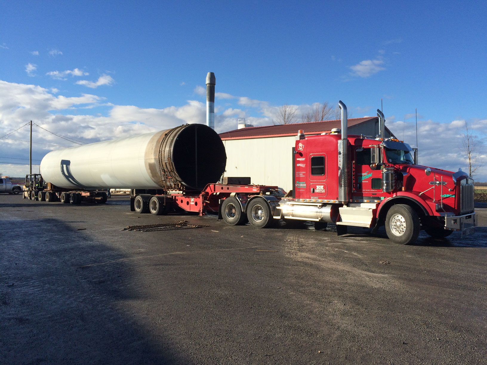 Un semi-remorque rouge transporte un gros tuyau sur une remorque.