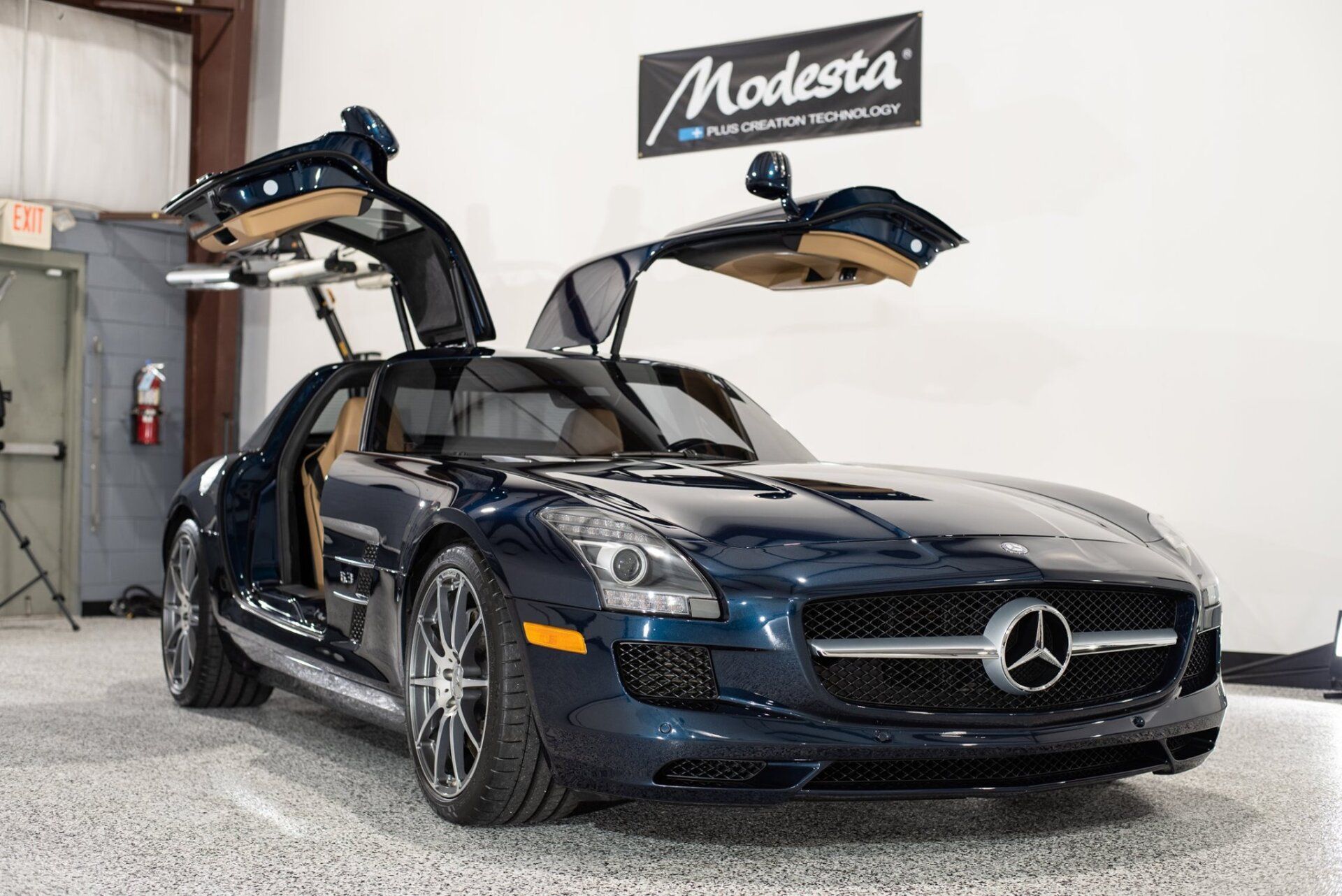 A blue mercedes benz sls is parked in a garage with its doors open.