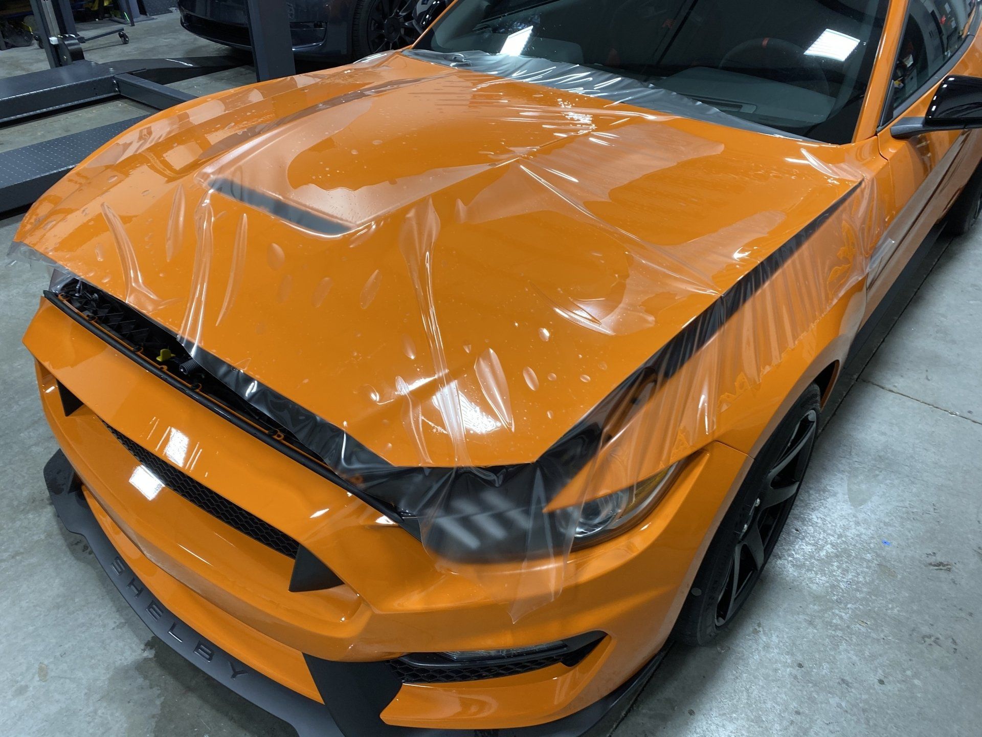 A close up of an orange ford mustang wrapped in plastic