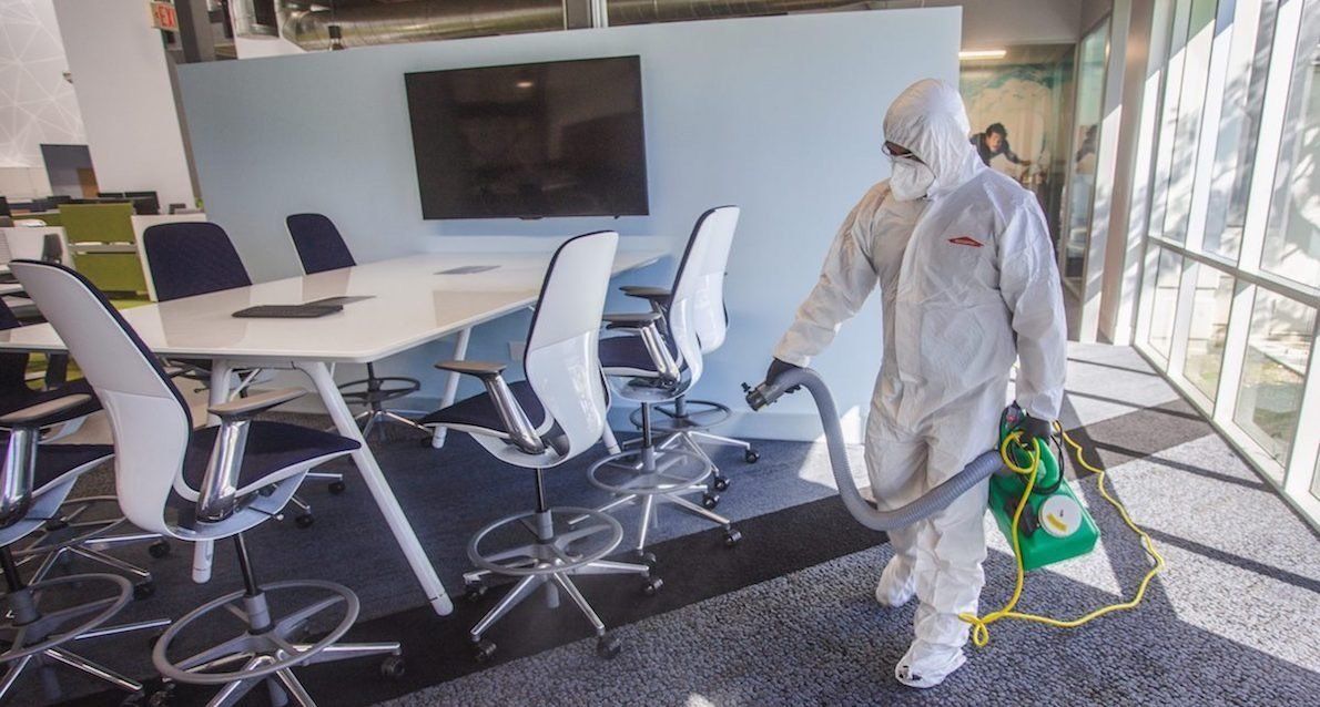 Person in hazmat suit disinfecting an office with spray equipment.