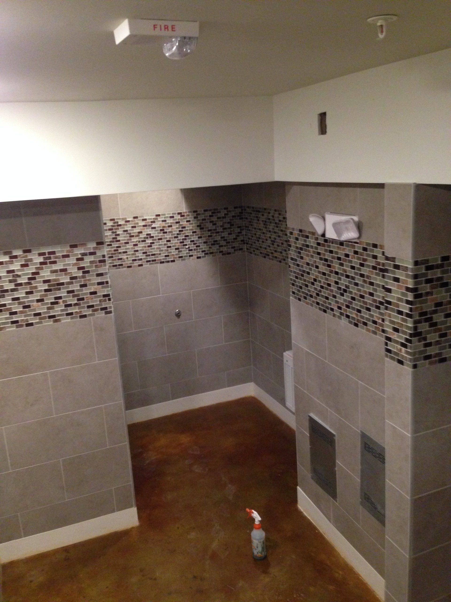 Bathroom with gray tile walls, brown floor, and decorative mosaic tile accents.