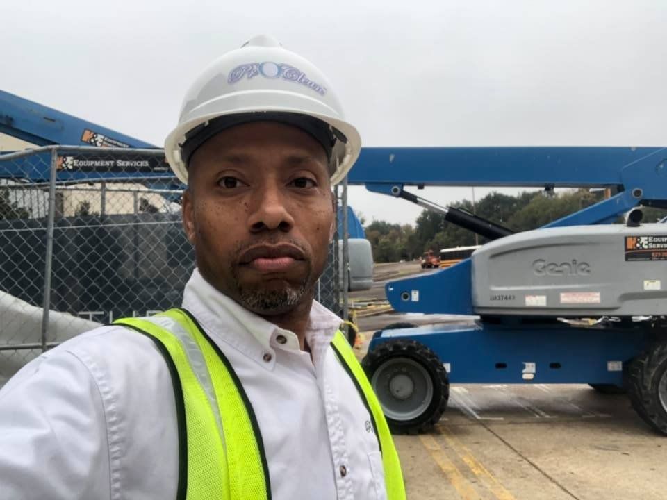 Construction worker in a white hard hat and vest, standing in front of a blue Genie lift.