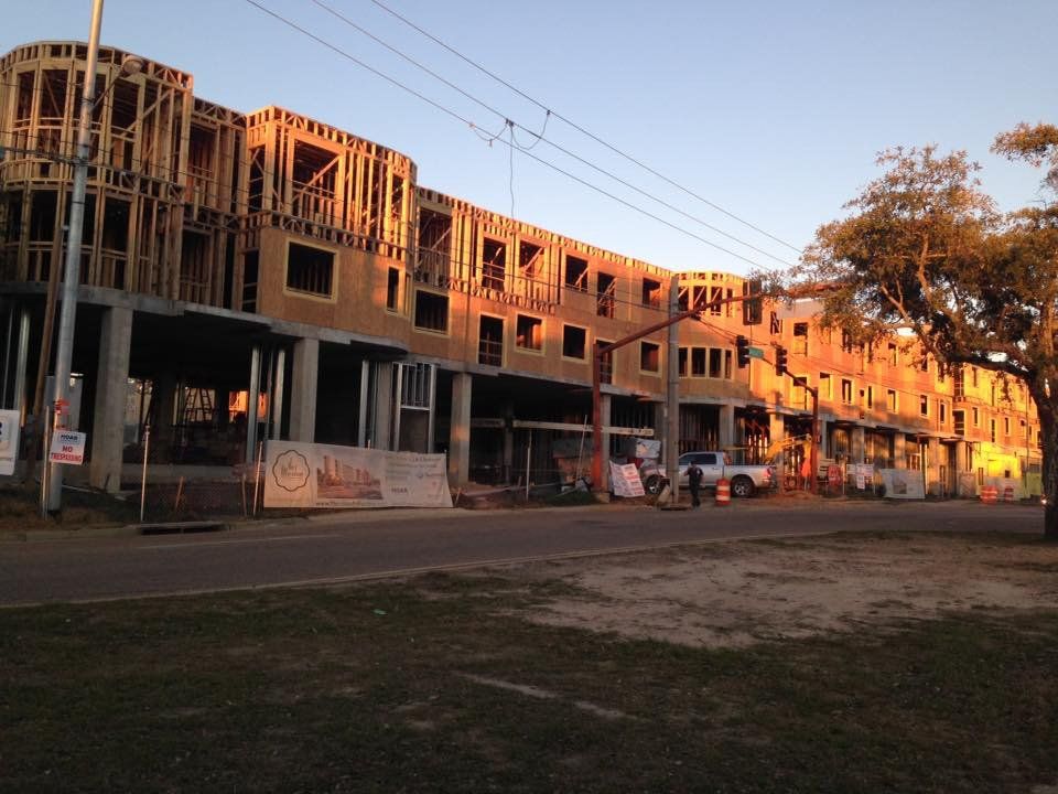 Building under construction; wood framing and concrete structure along a road at sunset.