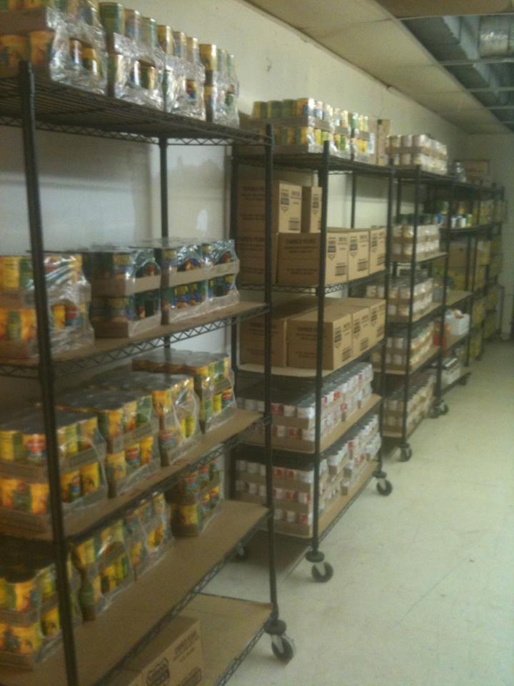 Shelves of packaged food items in a storage room. Metal shelving units are filled with canned goods and boxes.
