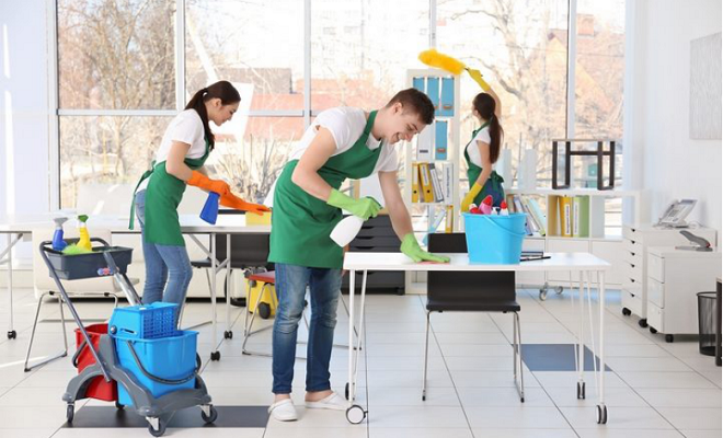 Office cleaning crew at work; two people wiping surfaces and a third dusting.