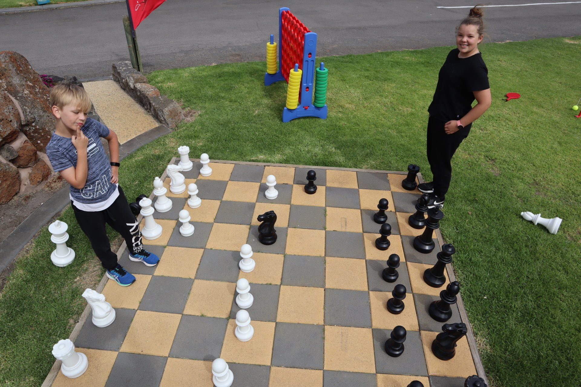 Girl and boy ponder their next moves as they play with a giant chess set at Gum Tree Caravan Park
