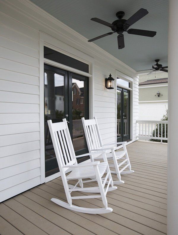 White rocking chairs on a covered porch with black ceiling fans and white siding