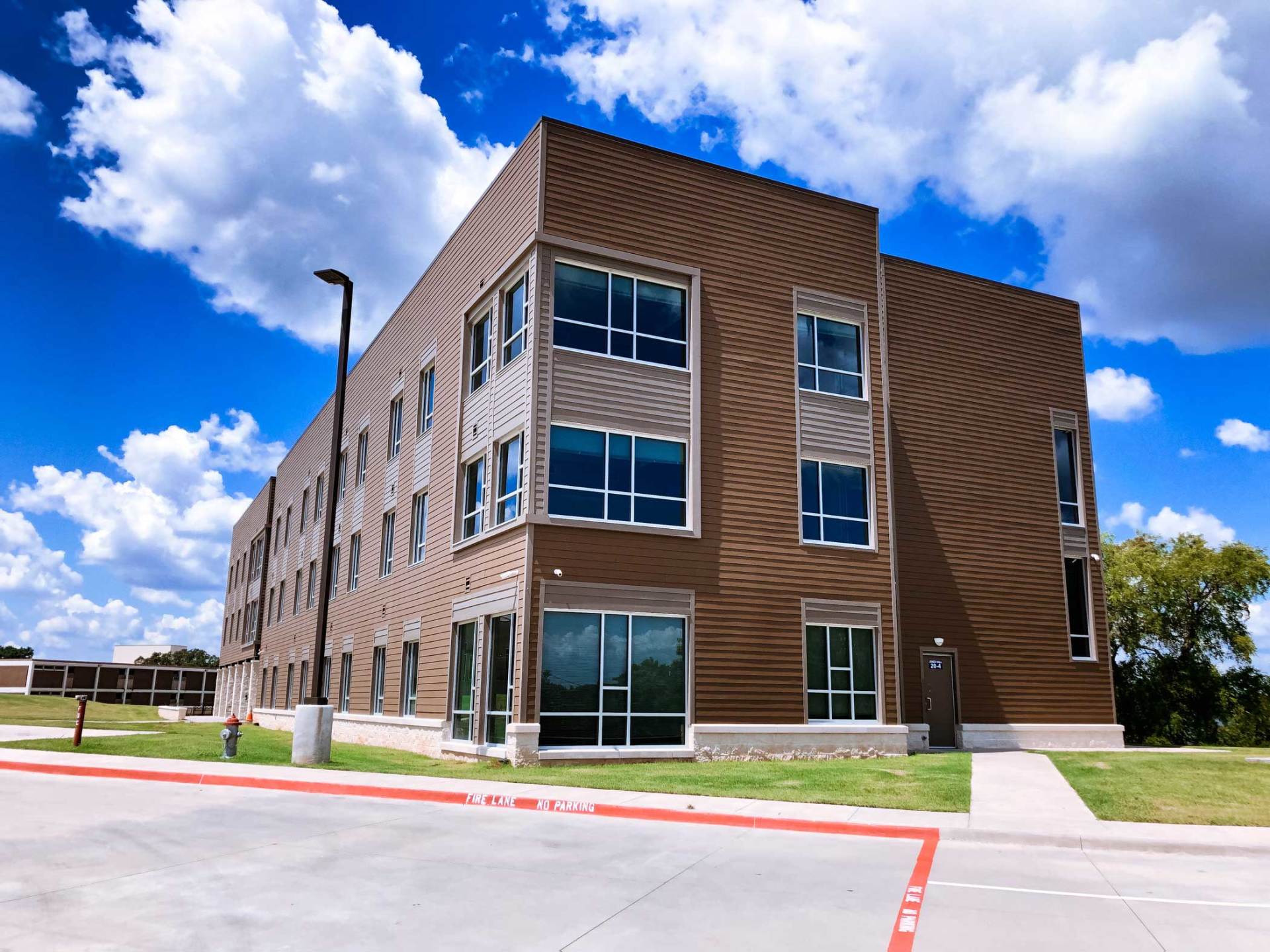 Modern three-story brick building with large windows under a blue, cloudy sky