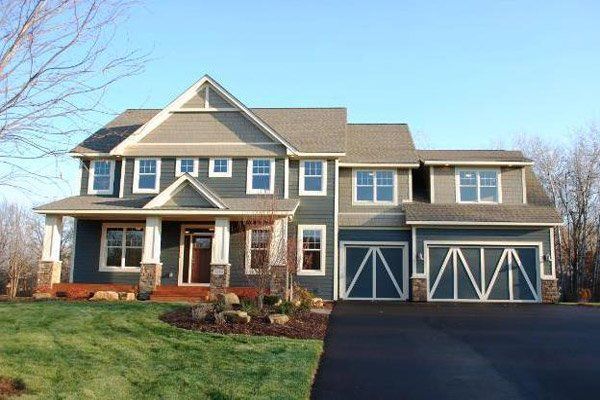 Large gray two-story suburban house with blue shutters, front porch, and two-car garage under clear sky