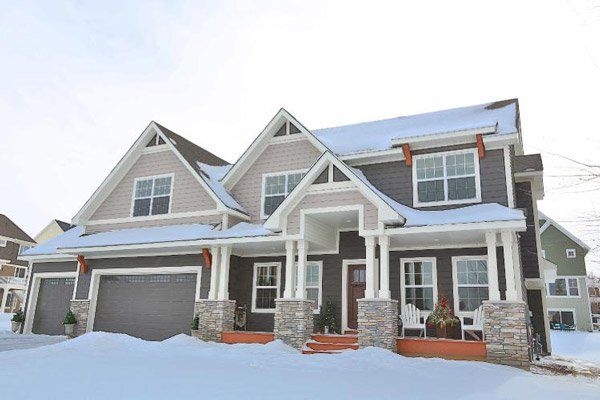 Snow-covered suburban house with gray roof, stone accents, and a two-car garage