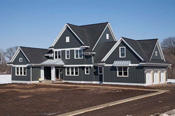 Large dark gray suburban house with white trim and a garage on a bare lot under a blue sky