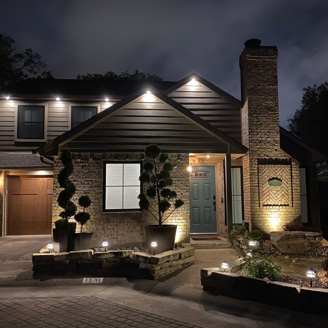 Illuminated brick house at night with stone chimney, garage, and lit front entry path